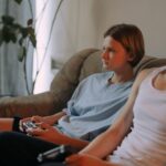 Dwóch nastolatków gra na PS4 w salonie, trzymając pady w dłoniach