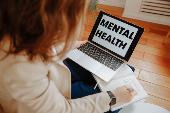 Kobieta na terapii online notuje, obok laptop z napisem Mental Health