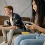 Młodzi dorośli grają razem na PS4 na kanapie w salonie