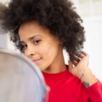 Pewna siebie kobieta z afro poprawia włosy, patrząc w lustro